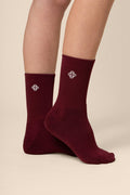 Maroon socks with a logo worn by a person on a beige background