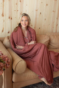 Model sitting on beige couch wrapped in Adult Quilted Blanket in Ember 2.5