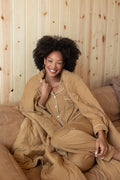 Model covered with Adult Quilted Blanket in Ochre 2.5 wearing Long sleeve women's pajama set in Ochre sitting on a beige couch