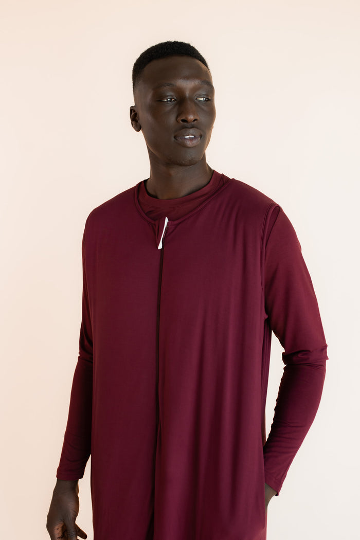 A man wearing a maroon sleep sack with a front zipper, photographed against a solid light beige background.