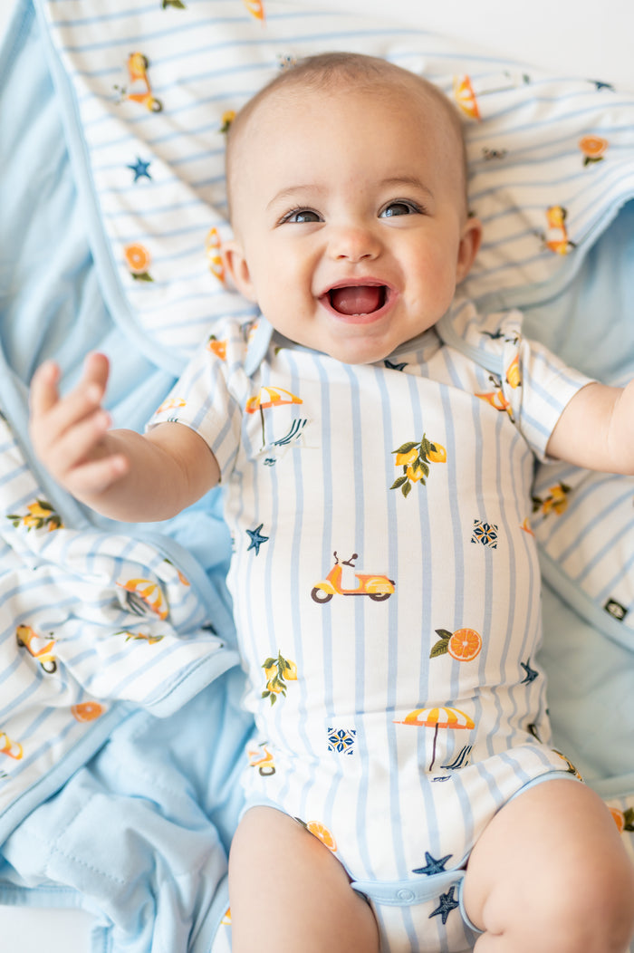 Close up of smiling baby laying on a Baby Blanket in Amalfi Coast 1.0 wearing the short sleeve bodysuit