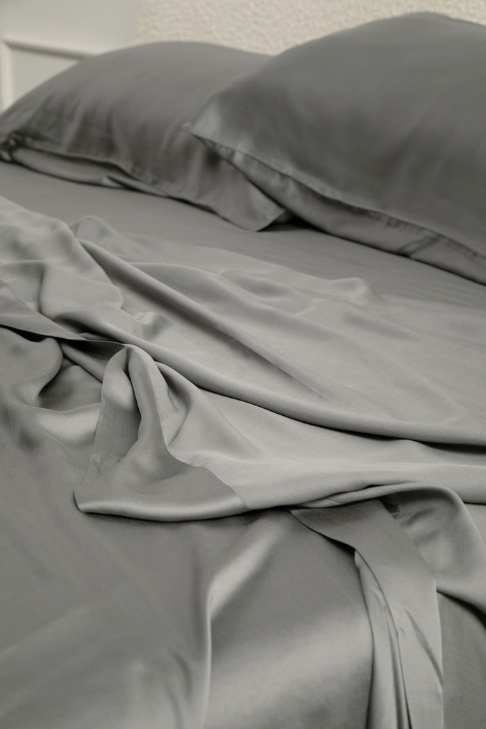 Close up of the Bamboo Sateen Pillowcase Set in Ash and matching bedsheets on a bed