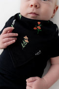 Baby wearing Bib in Midnight Wildflower print over a black bodysuit on a white background