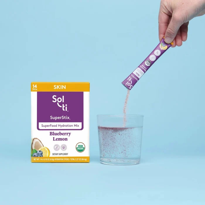 Hand pouring Sol-ti SuperStix Blueberry Lemon into a glass beside the product box
