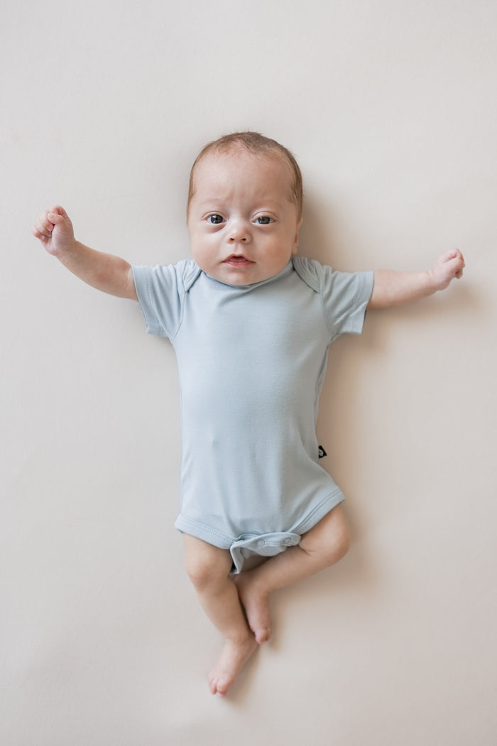 Baby wearing Bodysuit in Fog color on a beige background