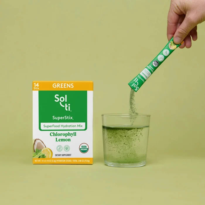 Hand pouring Sol-ti Greens SuperStix into a glass beside the product box