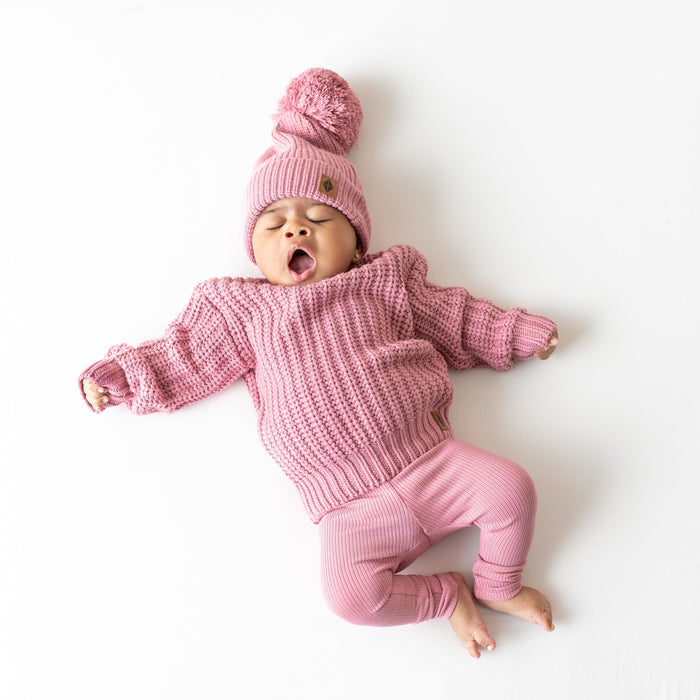 Infant wearing soft and stretchy Kyte Baby Chunky Knit Pom Beanie in Apple Blossom pink