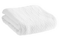 Displayed against a white background is the Cotton Thermal Blanket by 1888 Mills, featuring a folded, white knitted design crafted from premium 100% cotton. Its chevron pattern with raised zigzag lines enhances its cozy and warm appearance. The blanket boasts neatly finished edges and exudes a soft, hotel-quality allure that is inviting.