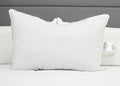 The Pillow Factory Downlite 50/50 Waterfowl Feather/Grey Down Pillow stands upright on a neatly made bed with a white quilt and gray upholstered headboard. Another medium support pillow is partially visible behind it.