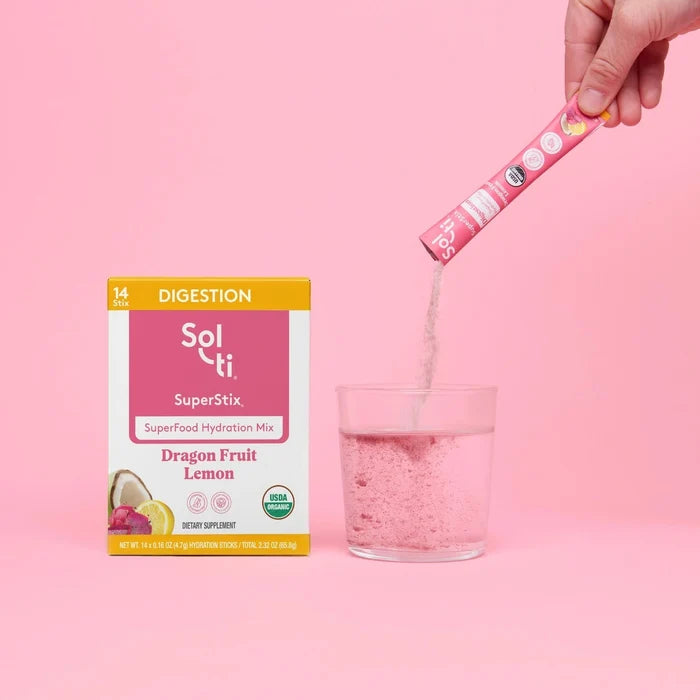 Hand pouring Sol-ti SuperStix hydration mix into a glass beside the product box