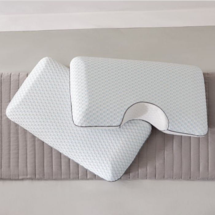 Two rectangular EverRest Bamboo Charcoal Pillows with cooling covers by Malouf, in white with light blue geometric patterns, rest on a quilted gray mat. One pillow features a curved notch for neck or shoulder support in a minimal, clean setting.
