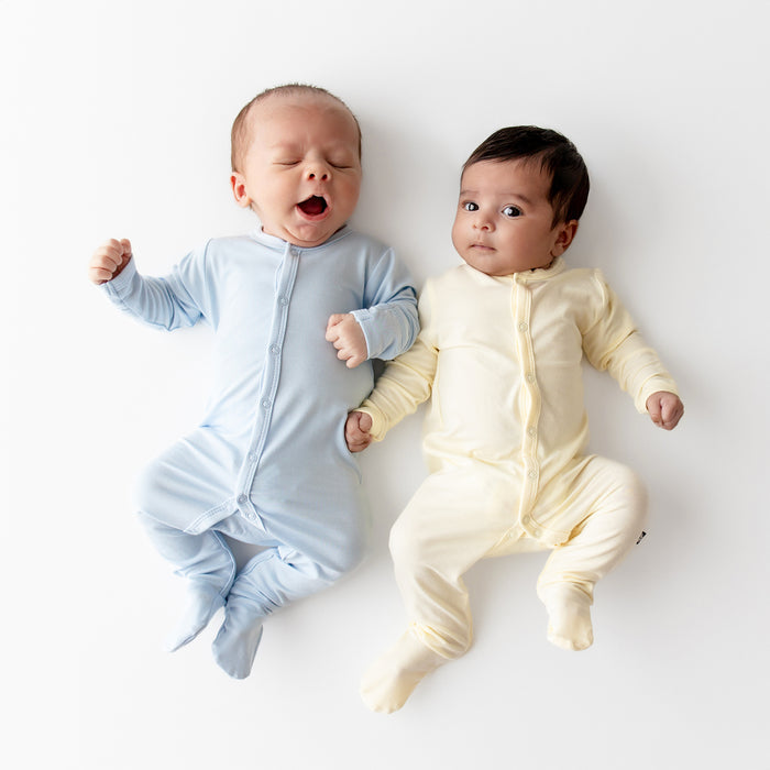 Two babies wearing light blue and yellow footies on a white background