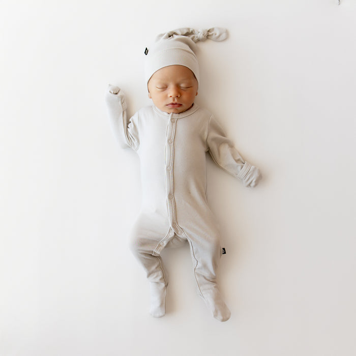 Baby in a snap footie in a creamy light grey with matching knotted cap