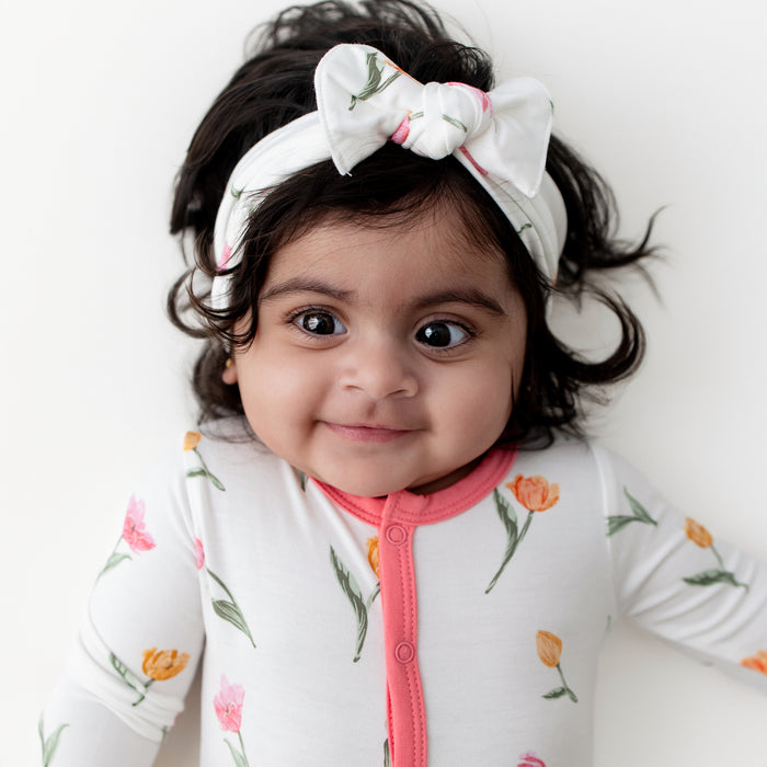 Close up of infant modeling the Footie in Tulip and matching knotted bow headband