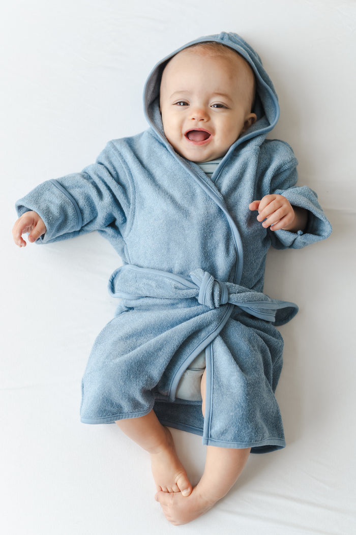 Infant laying on a bed wearing the Hooded Bath Robe in Slate
