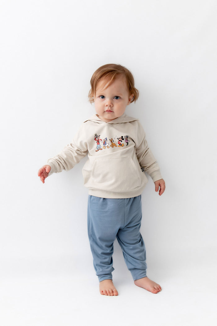 Toddler standing wearing mickey mouse  friends hoodie with blue pants.