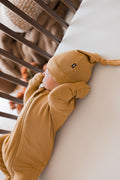 Baby wearing Knotted Cap in Ochre with zippered footie in Ochre lying in a crib