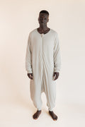 A man wearing a light beige, full-body zip-up harem sleep sack against a solid, warm off-white background.