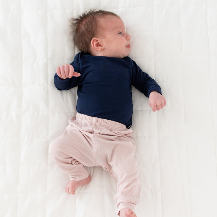 Newborn wearing Kyte Baby Long Sleeve infant Bodysuit in Navy and Pants in Oat