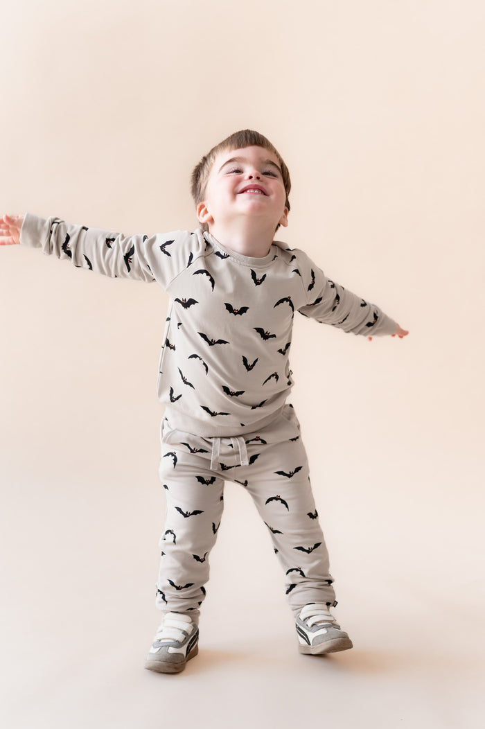 Boy in Long Sleeve Jogger Set in Bats print and  shoes on a beige background