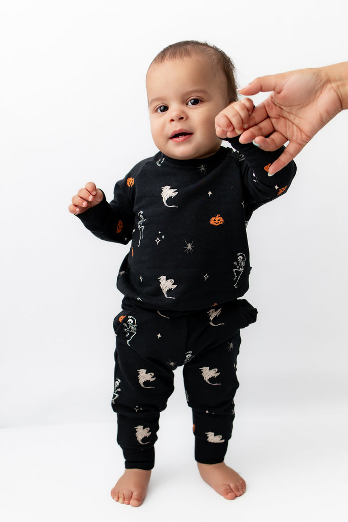 Baby wearing Long Sleeve Jogger Set in Halloween Friends print standing holding an adult's hand on a white background