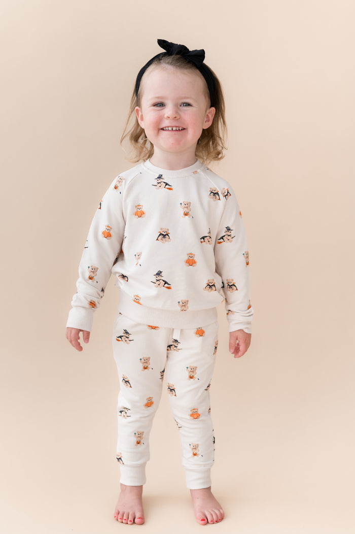 Girl posing in Beige Long Sleeve Jogger Set in Halloween Teddy print with a black bow on a beige background