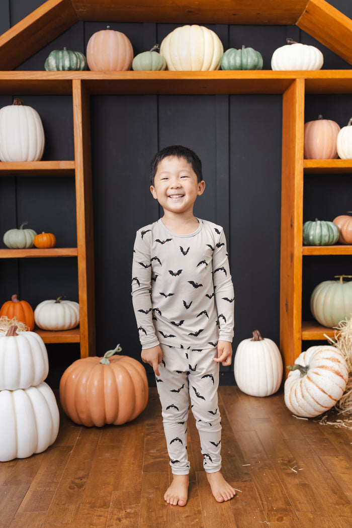 Boy wearing Long Sleeve Pajamas in Bats print standing in front of pumpkin decorations