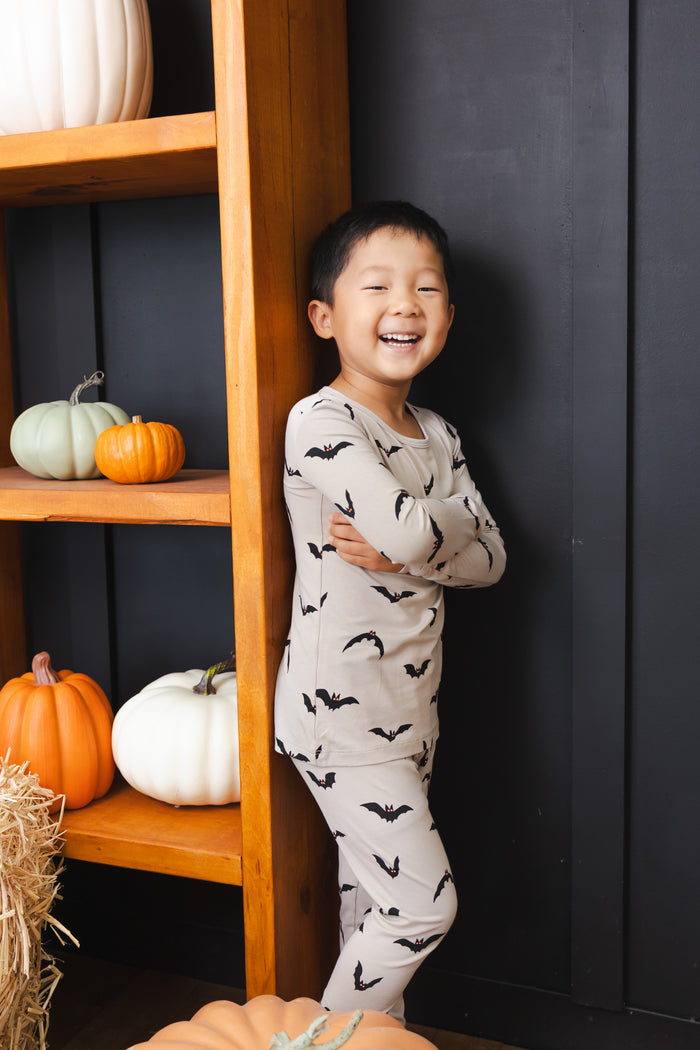 Boy smiling Long Sleeve Pajamas in Bats print standing against a shelf with pumpkin decorations