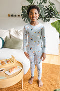 Child smiling in ice sushi pajama se, standing next to a table of sushi with a plant in the background