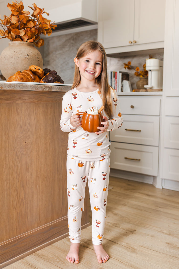 Girl standing in kitchen wearing Long Sleeve Pajamas with Pumpkin Spice Latte print holding a spice latte cup.