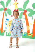 Girl posing in Long Sleeve Skater Dress in Curious George print with a red bow on head standing in front of a colorful background