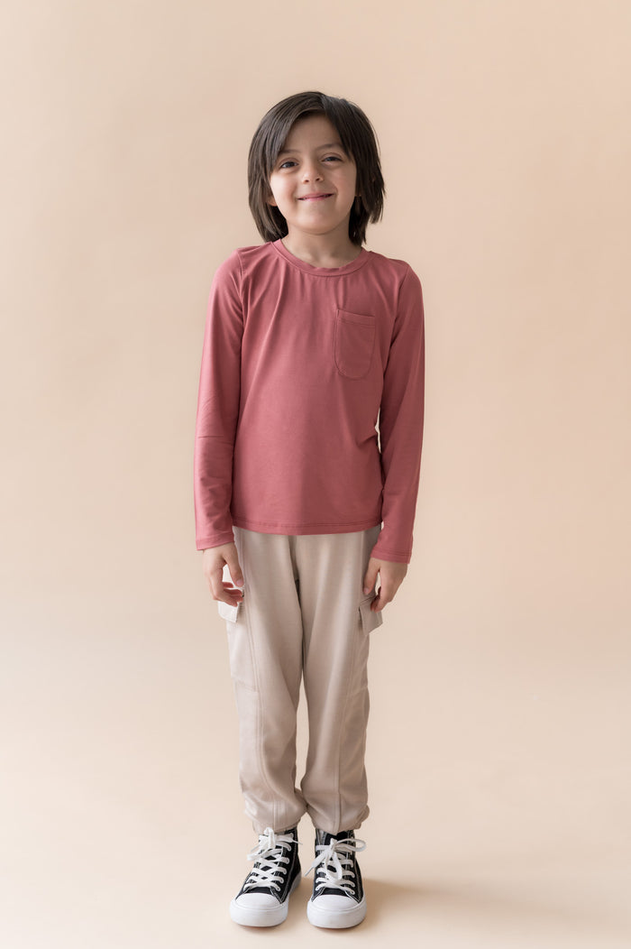 Boy standing in Long Sleeve Toddler Crew Neck Tee in Ember over a beige pants on a beige background