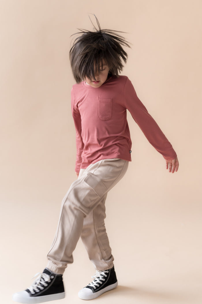 Boy posing in Long Sleeve Toddler Crew Neck Tee in Ember over a beige pants