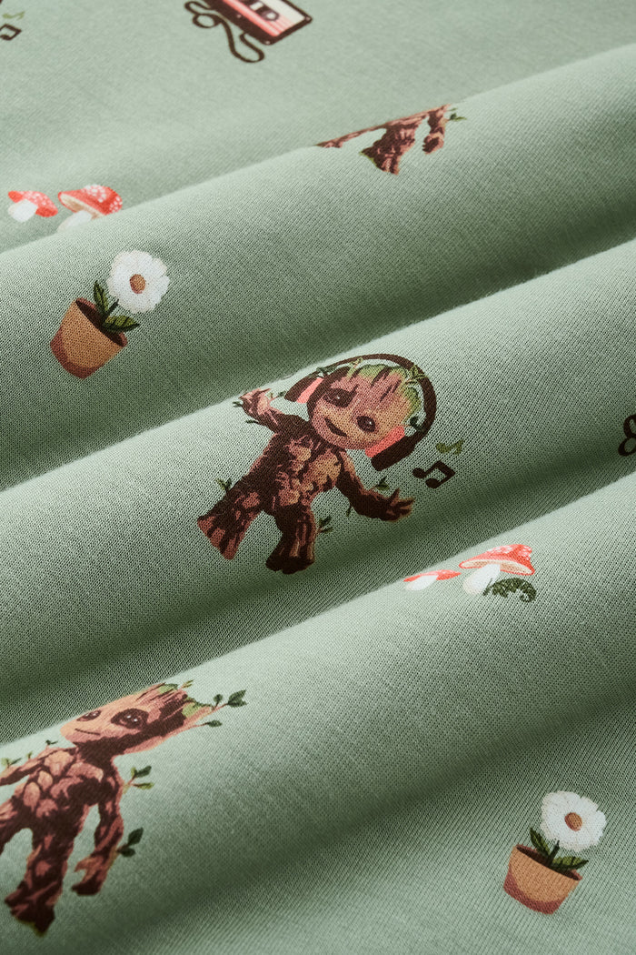 A repeating, all-over print featuring: a standing Baby Groot; a dancing Baby Groot wearing headphones and listening to music; a potted white daisy flower; two toadstools with red caps and white spots; a cluster of ivy; and a cassette tape with tape pulled out, over a dusty sage green background color named Thyme.