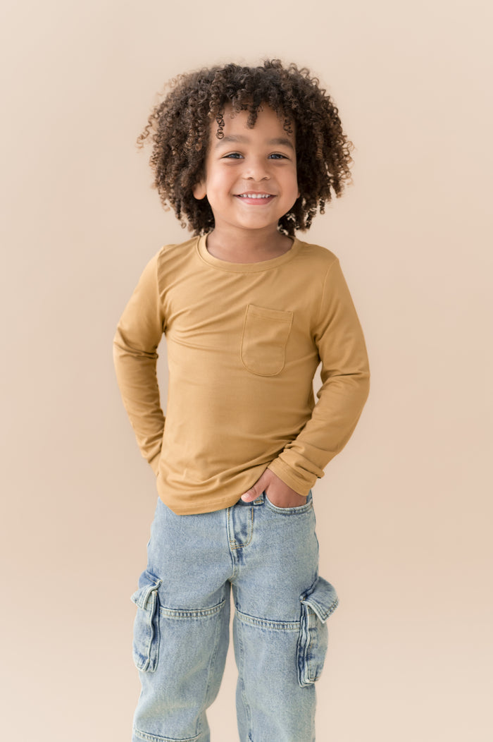 Boy wearing Long Sleeve Toddler Crew Neck Tee in Ochre over blue jeans on a beige background