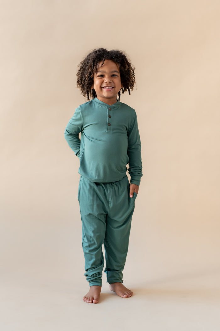 Boy wearing Long Sleeve Toddler Henley Tee in Pine over Toddler Jogger pant on a beige background