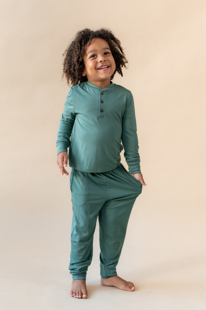 Boy wearing Long Sleeve Toddler Henley Tee in Pine over Toddler Jogger pant on a beige background