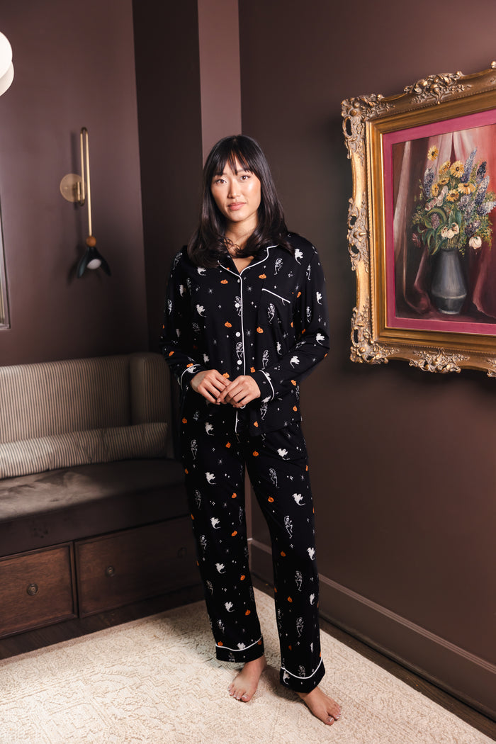 Modal wearing Black Long-Sleeved Women's Pajama Set in Halloween Friends print standing in a living room