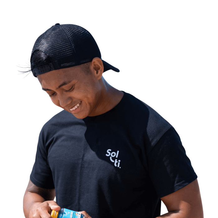 A man wearing a black Sol-ti organic cotton t-shirt and a black cap, holding a Sol-ti SuperShot shown against a light background.