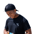 A man wearing a black Sol-ti organic cotton t-shirt and a black cap, holding a Sol-ti SuperShot shown against a light background.