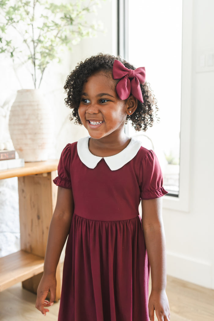 Girl smiling in Peter Pan Collar Dress in Burgundy with Medium Alligator clip bow