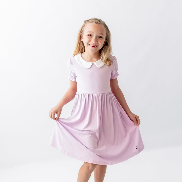 Young girl posing modeling the Peter Pan Collar Dress in Thistle in front of a white background