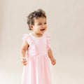 Child wearing a pink dress with ruffled sleeves against a plain background