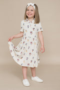 Young girl wearing a cream dress with colorful mickey and friends pattern on a beige background