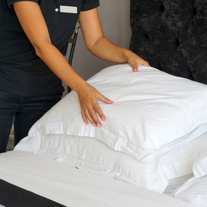 A woman is arranging Restful Nights Trillium Pillows on a bed.