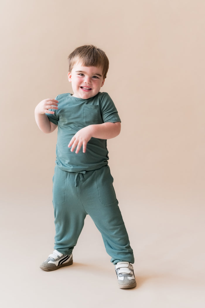 Child smiling in Ribbed Jogger Pant in Pine on a beige background
