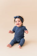 Baby sitting in Ribbed Leggings and knotted bow head band in Oxford on a beige background