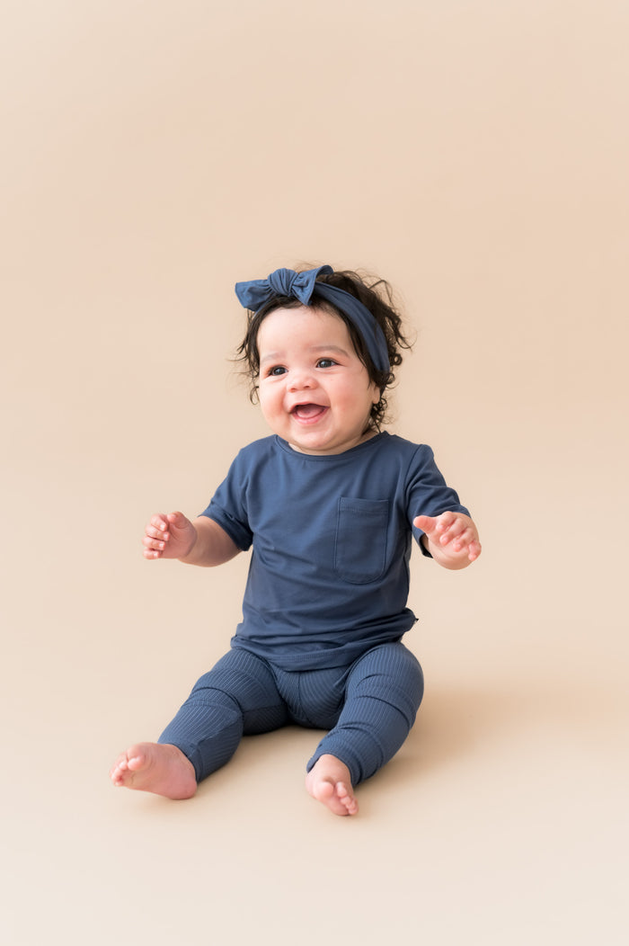 Baby sitting in Ribbed Leggings and knotted bow head band in Oxford on a beige background