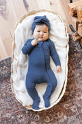 Baby wearing Ribbed Zipper Footie and Ribbed Headwrap in Oxford lying in a basket