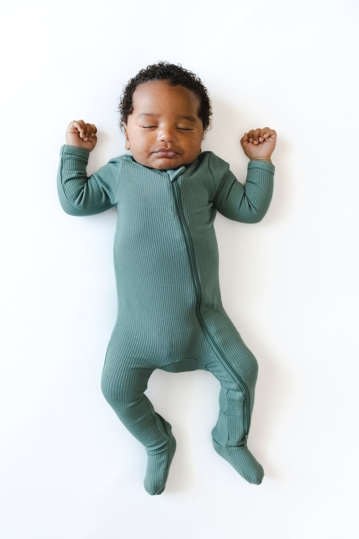 Baby sleeping in Ribbed Zipper Footie in Pine on a white background